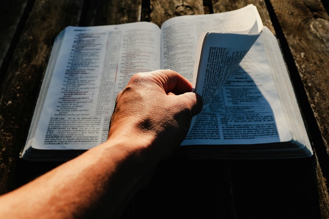 a person holding an open book on top of a wooden table